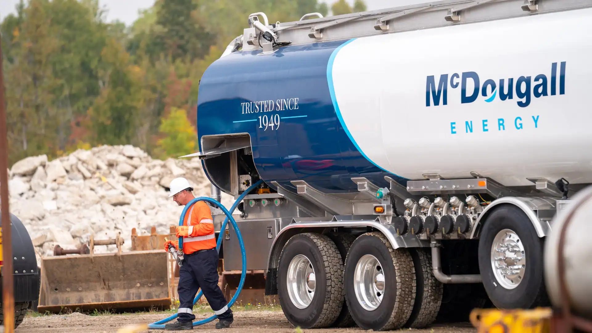 Fuel delivery truck at McDougall Energy fueling station with a worker in safety gear.