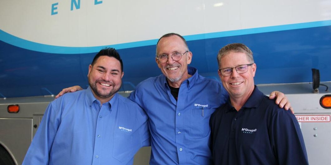 Three McDougall Energy Employees smiling closely together in front of a blue and white wave background
